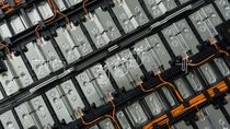 Primo piano dell’interno di una batteria EV, che mostra i fili arancioni che collegano e conducono l’elettricità attraverso una serie di diverse piastre metalliche. 