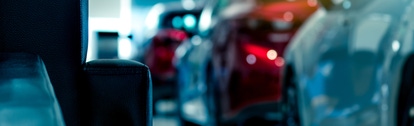 Blurred new luxury red and gray car parked in modern showroom. Selective focus on black leather sofa in modern showroom. Car dealership. Showroom interior. Automotive industry on coronavirus crisis.